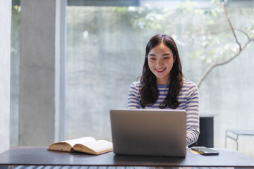 Smiling student working on laptop with open book nearby