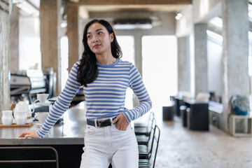 Young asian barista woman leaning on the counter in a modern coffee shop