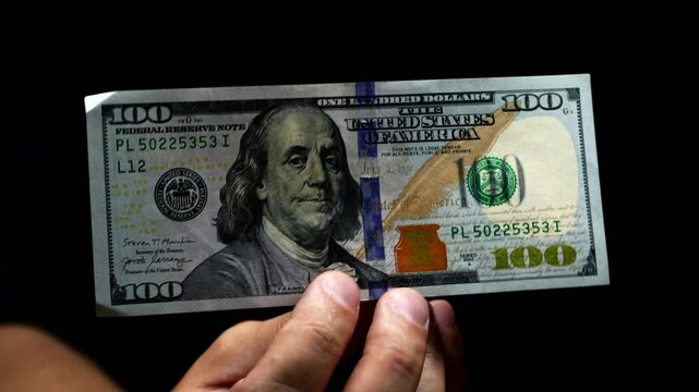 A man holds one hundred American dollars on a black background.
Paper money and business and finance concept.
Money savings in hands close-up.
Man receives salary at work