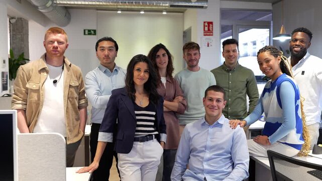 Young professionals standing together, smiling confidently during group photo shoot in contemporary, bright office workspace, capturing team spirit and collaborative energy