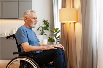 Senior man sitting in wheelchair looking out window at home
