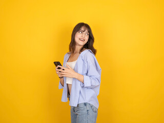 Side view profile portrait of woman using holding mobile phone smiling cheerful looking back at copy space workspace area standing isolated on yellow studio background. Wear white top, shirt and jean.