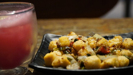 A plate of gnocchi with vegetables served alongside a refreshing drink in a cozy setting. Perfect...