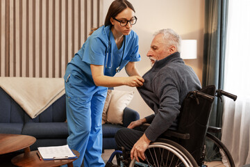 Beautiful nurse assisting elderly man in wheelchair at home