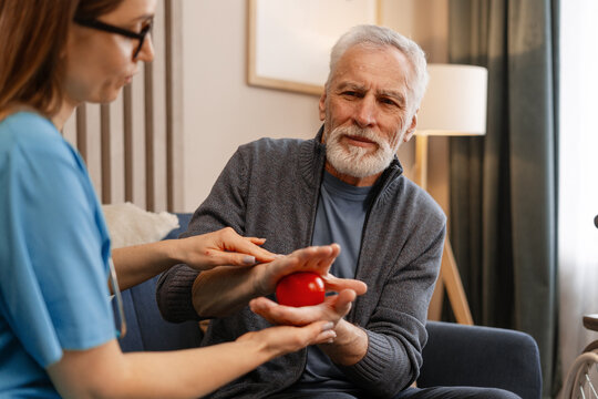 Nurse assisting elderly man with hand rehabilitation exercises at home