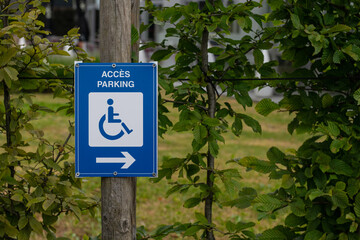 A blue sign among natural greenery indicating a parking space suitable for disabled access, marked with a white wheelchair symbol.