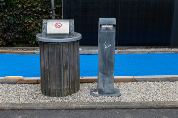 Dual-purpose trash and cigarette waste bin placed on gravel.