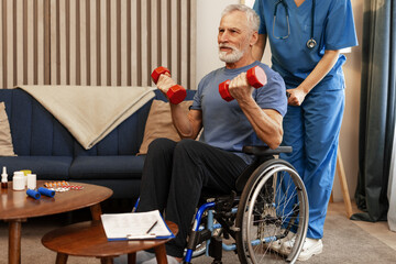 Senior man lifting weights with nurse assistance in living room sitting in wheelchair