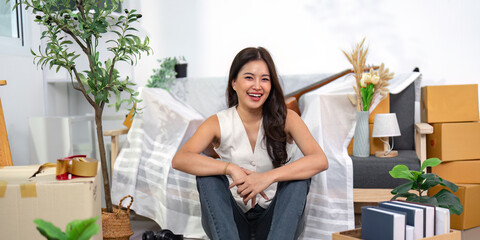 Moving house. Smiling woman sitting on the floor surrounded by boxes and plants.
