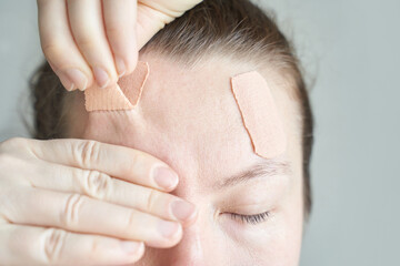 Asian adult female applying cosmetic patches for facial skin care and wrinkle treatment.