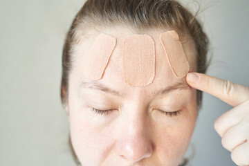 Female caucasian adult with facial patches on forehead for skin care or wound healing.