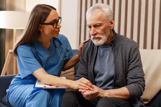 Female doctor comforting sad senior man at home visit