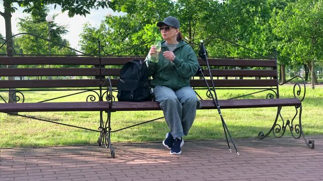 Woman Relaxing in Park Drinking Water During Nordic Walking Workout Break. 4K Video.