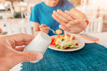 Woman refusing salt shaker while having lunch at restaurant, healthy eating and lifestyle concept