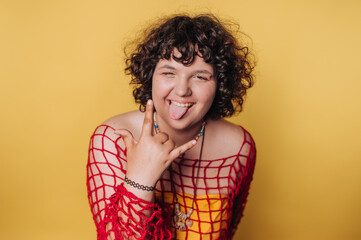 Young person showing playful gesture in colorful outfit against bright yellow backdrop during a casual indoor event