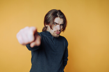 Young man pointing assertively against a vibrant yellow background in a casual pose
