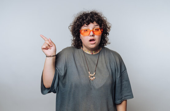 Person with curly hair gestures emphatically while wearing bright orange sunglasses in a neutral setting during daylight