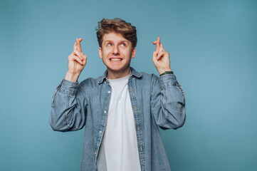 Man with an optimistic expression making a wish with crossed fingers against a blue background