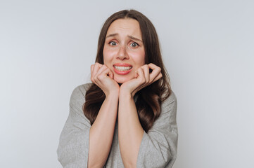 Young woman displays signs of anxiety while sitting against a plain background in a casual gray...