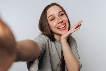 Smiling young woman taking a self-portrait with cheerful expression in a light-colored room while...