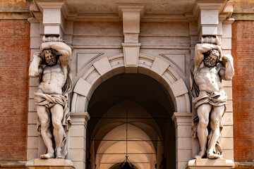 Two muscular caryatid statues holding up a classical portico in historic Italian building.
