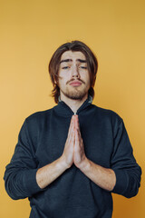 Young man expressing gratitude with hands together against a bright yellow backdrop