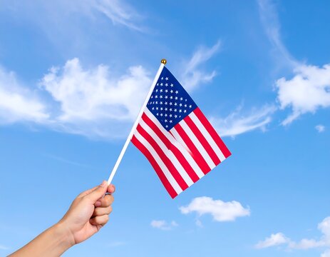 Hand holding a small US flag against a partly cloudy sky