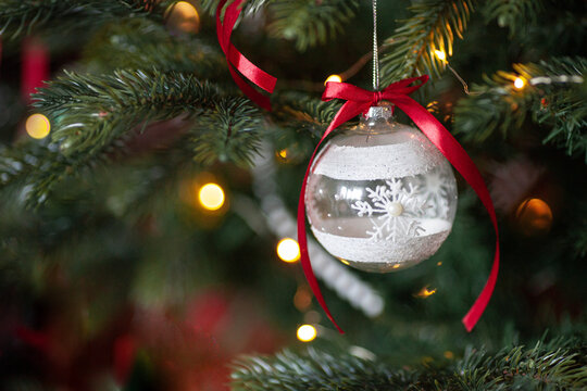 Close up of glass ball - christmas tree decoration with white snowflake and red ribbon. Christmas and new year background. Festive atmosphere.
