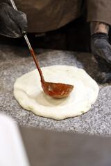 maestro pizzero vertiendo tomate en la masa de una pizza artesanal