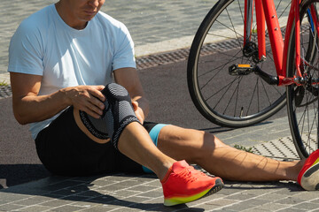 Cyclist fell off his bike and injured his knee. Unhappy cyclist with knee pain and injury outdoors. Close up.