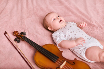 Baby girl, light hair, lying on soft pink blanket beside violin. Calm expression, cozy ambiance...