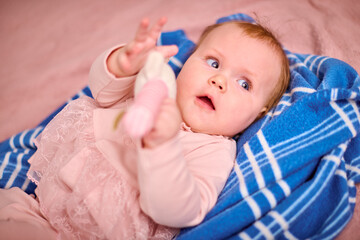Young female child with light hair and fair skin lying on blue blanket. Holding plush toy while...