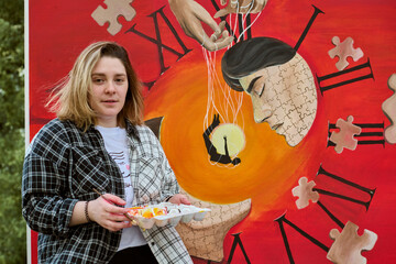 Young woman holding paint palette stands by vibrant surreal clock painting with puzzle patterns....
