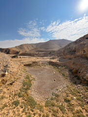 Dry, cracked ground in an arid valley near Shunah al-Janubiyah, Jordan, with surrounding desert hills and a clear blue sky.