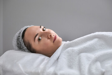 Mature woman in spa setting wears towel and hair cap, exuding comfort and relaxation. Serene...