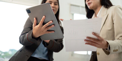 Collaboration and Success. Two businesswomen discussing project details with tablet and documents.
