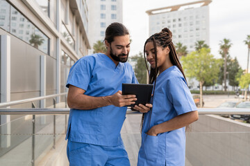 Two Multiracial diverse healthcare workers consulting a digital tablet outside a hospital building