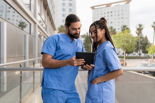 Two Multiracial diverse healthcare workers consulting a digital tablet outside a hospital building - Powered by Adobe