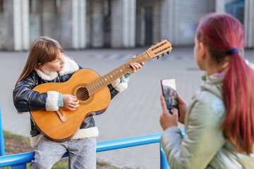 Focused girl playing guitar while being filmed outside