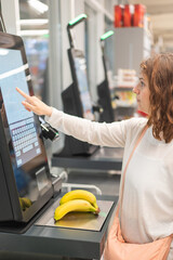 Caucasian woman using self-checkout technology at grocery store. 
