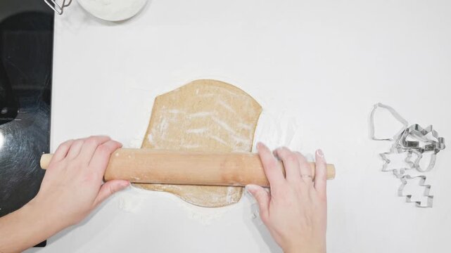 Hands roll out gingerbread dough on a floured surface, surrounded by cookie cutters. The scene captures the joy and creativity of holiday baking traditions