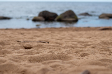 Low-angle view of textured beach sand in focus, with large sea rocks and calm water blurred in the...