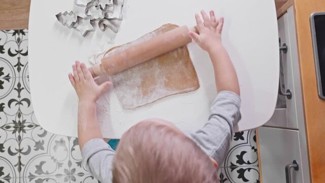 A toddler rolls gingerbread dough in a warm kitchen setting, preparing for holiday cookies. The playful moment highlights the joy of family bonding during seasonal baking