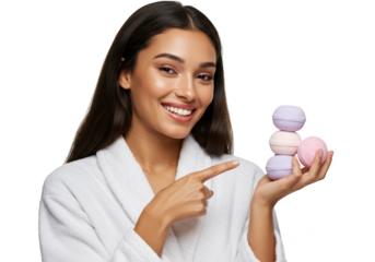 A smiling woman in a white robe points to a stack of colorful bath bombs she holds in her hand, isolated on a transparent background
