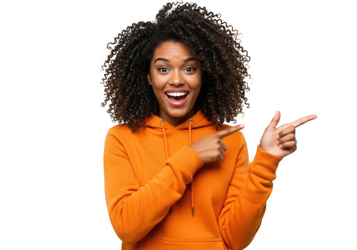 An excited young african woman in an orange hoodie points forward with a smile, isolated on white isolated on transparent background