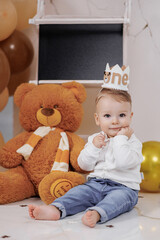 Cute toddler celebrating first birthday with teddy bear in decorated room