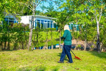 A janitor cleans the lawn area from leaves and mown grass. Hotel cleaning service.