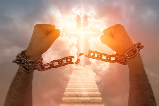 Men's hands breaking chains against the sky with a luminous cross. Concept of christian religion