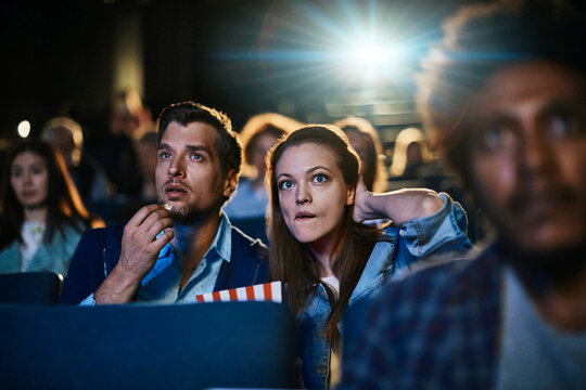 Young couple watching a movie and eating popcorn in a movie theater
