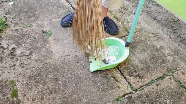 Sweeping up trash using a broom and dustpan in the yard